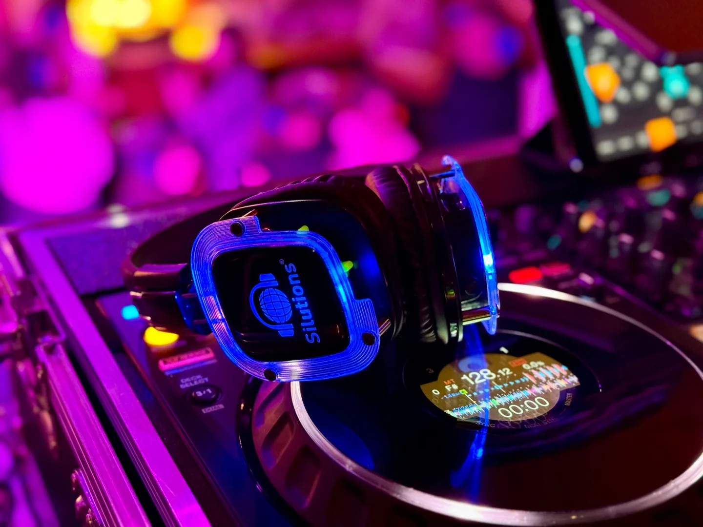 Leuchtender Silent-Disco-Kopfhörer auf dem DJ-Pult vor buntem Partylicht