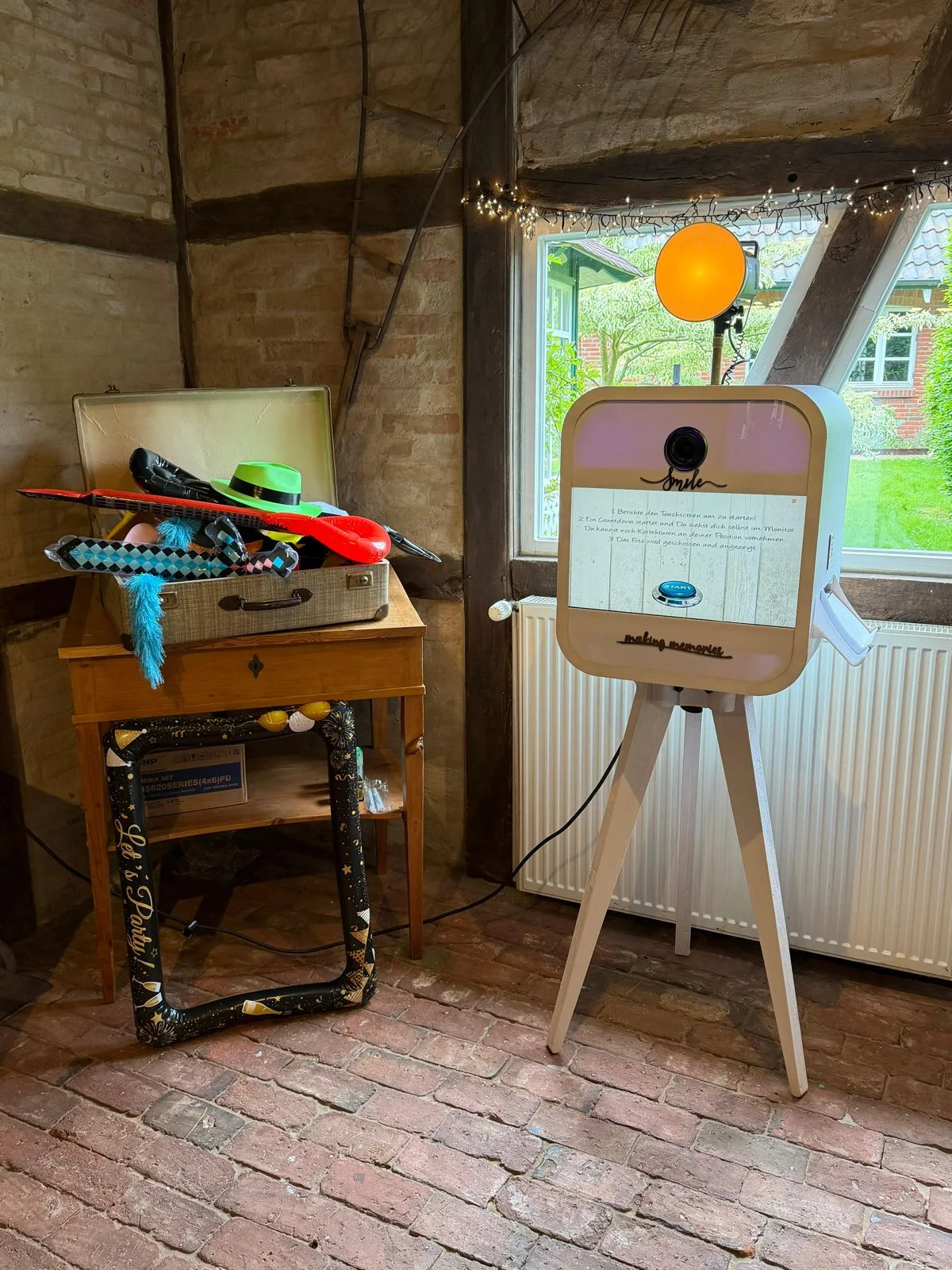 Fotobox auf weißem Stativ mit Blitz und Accessoires in einer rustikalen Location